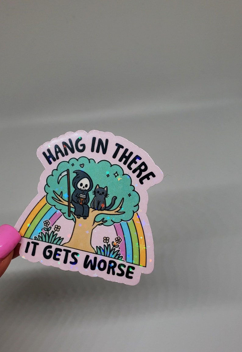 Op de afbeelding: Een roze holografische sticker met een regenboog en een cartoon grim reaper die op een boom zit met een kat. De tekst op de sticker luidt "Hang in there it gets worse".