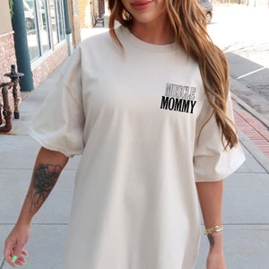 May include: A light beige oversized t-shirt with the text "MUSCLE MOMMY" printed on the front.