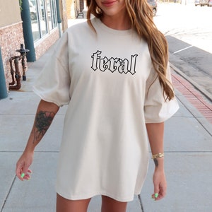 Pu&ograve; includere: Una maglietta oversize beige con la parola "feral" stampata in lettere gotiche nere.