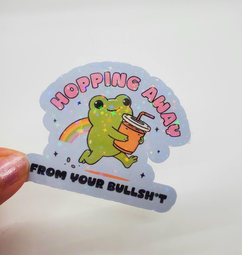 May include: A holographic sticker with a cartoon frog holding a cup of orange juice. The frog is running and the text says "Hopping Away From Your Bullsh*t".