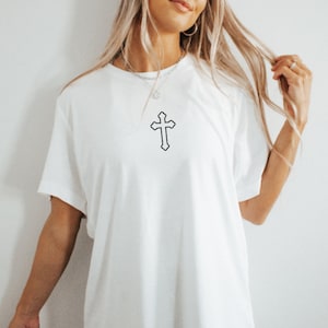 May include: A white oversized t-shirt with a simple black outline of a cross on the front.