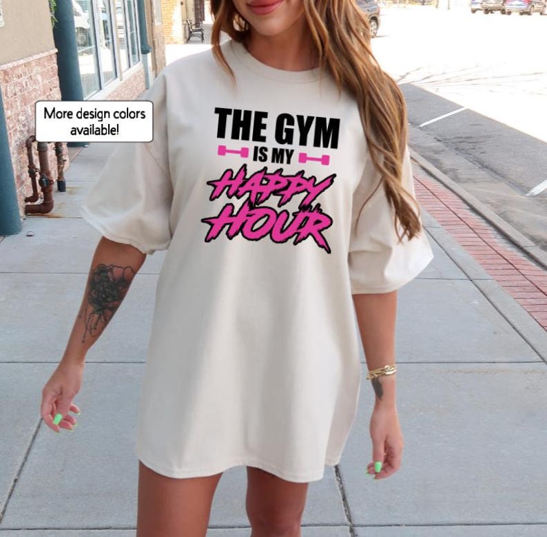 Peut inclure: Un t-shirt blanc surdimensionn&eacute; avec le texte "The Gym is my Happy Hour" en lettres noires et roses. Le texte est dans une police de caract&egrave;res graphique et audacieuse.