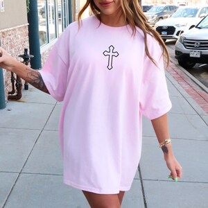 May include: A pink oversized t-shirt with a black cross graphic on the front.