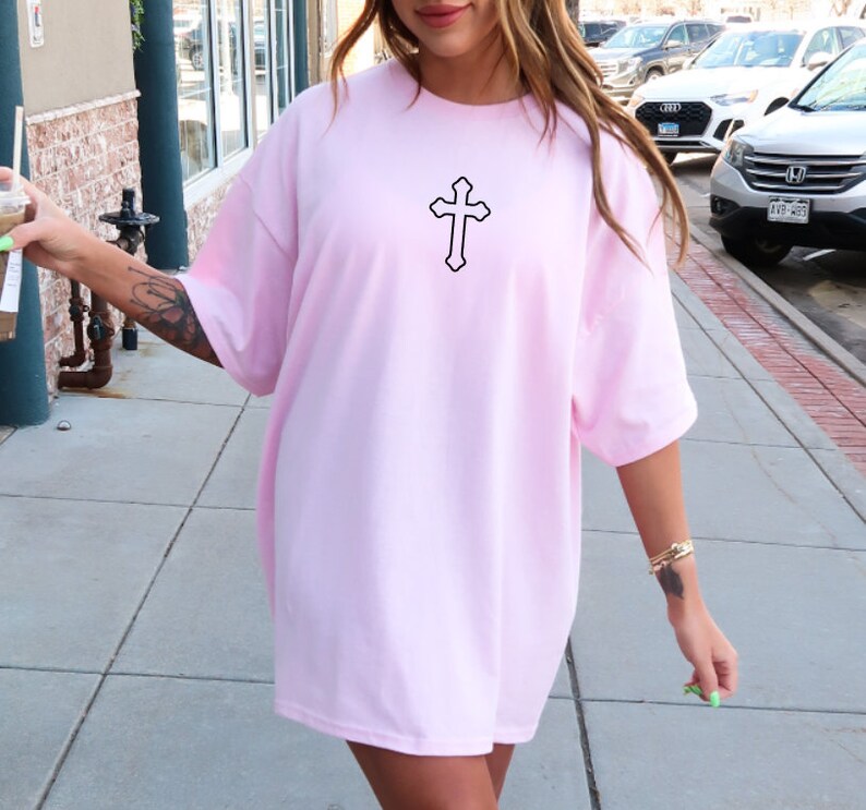 May include: A pink oversized t-shirt with a black cross graphic on the front.