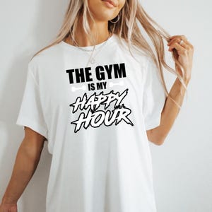 Peut inclure: T-shirt blanc avec un texte noir qui dit "The Gym is my Happy Hour".
