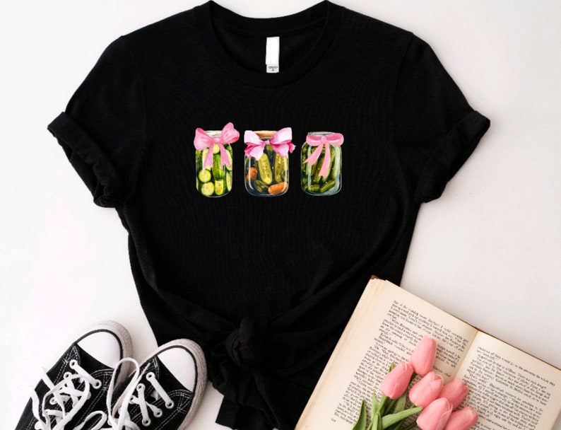 Pode incluir: Camiseta preta com um gr&aacute;fico de tr&ecirc;s frascos de picles amarrados com fitas cor-de-rosa. Os frascos est&atilde;o cheios de picles verdes e est&atilde;o dispostos em uma fila.