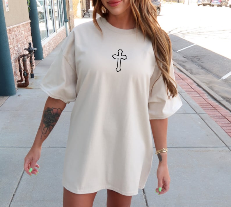 May include: A cream-colored oversized t-shirt with a black outline of a cross on the front.