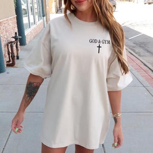May include: A cream-colored oversized t-shirt with the text "GOD & GYM" and a cross graphic.