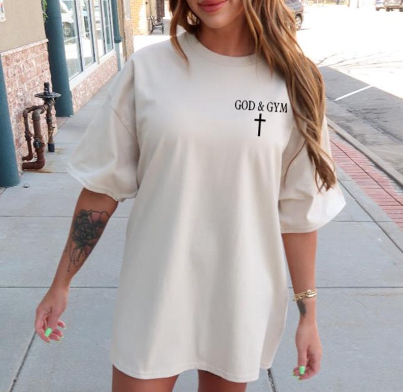 May include: A cream-colored oversized t-shirt with the text "GOD & GYM" and a cross graphic.