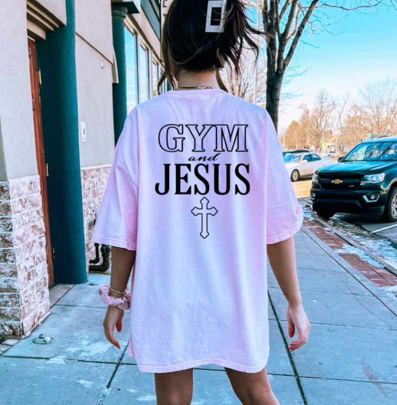 May include: A pink oversized t-shirt with the text "GYM and JESUS" and a cross printed on the back.