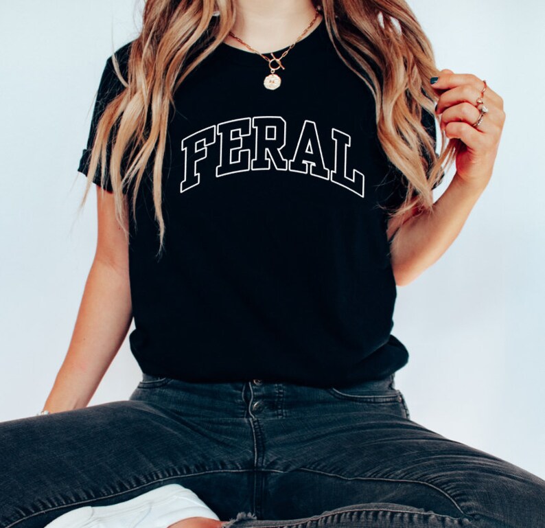 Może przedstawiać: Czarny T-shirt z nadrukiem słowa "FERAL" białymi literami z obramowaniem.