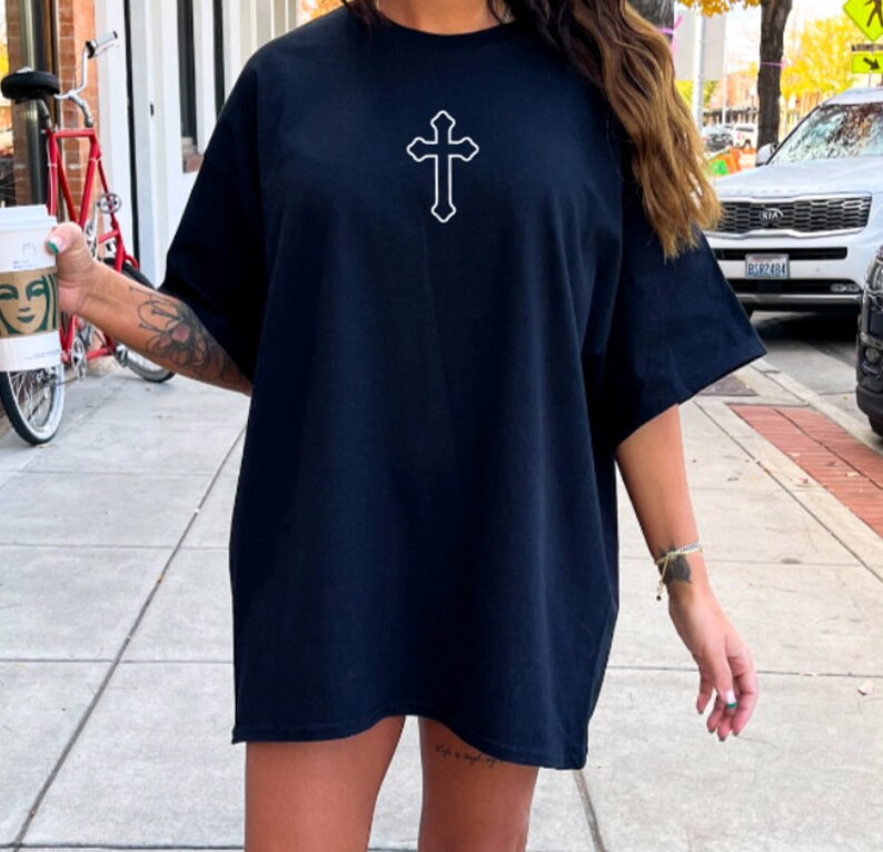May include: A black oversized t-shirt with a white outline of a cross on the front.