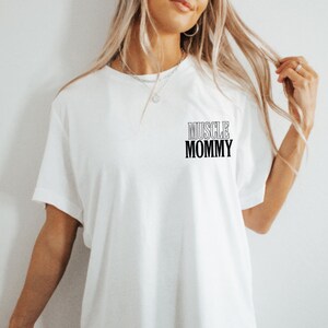 May include: White t-shirt with black text that reads "MUSCLE MOMMY" on the front.