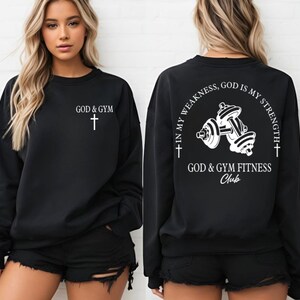 May include: Black sweatshirt with white text and a cross on the front. The back of the sweatshirt has a white graphic of dumbbells with the text "In my weakness, God is my strength + God & Gym Fitness Club".