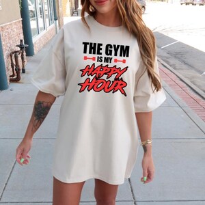 Peut inclure: Un t-shirt blanc surdimensionn&eacute; avec un motif rouge et noir qui dit "The Gym is my Happy Hour".