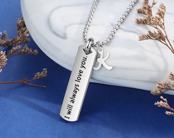 May include: Silver necklace with a rectangular pendant that says "I will always love you." The pendant has a small charm in the shape of the letter "K" hanging from it.