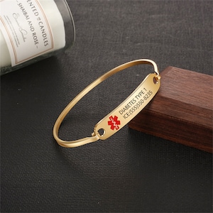 Puede incluir: Pulsera de alerta médica de oro con un símbolo médico rojo y el texto "DIABETES TYPE 1 ICE:(555)550-8235".