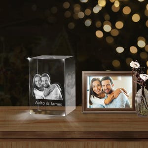 May include: A crystal cube with a 3D engraved photo of a couple, with the text "Aalto & James" and a date below the photo. A framed photo of the same couple is on the table next to the crystal cube.
