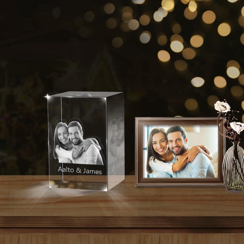 May include: A crystal cube with a 3D engraved photo of a couple, with the text "Aalto & James" and a date below the photo. A framed photo of the same couple is on the table next to the crystal cube.