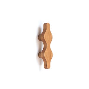 May include: A wooden cabinet knob with a unique wavy design. The knob is light brown and has two small round knobs on the sides.