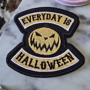 May include: Black and gold embroidered iron-on patch with a grinning jack-o'-lantern and the text "EVERYDAY IS HALLOWEEN".