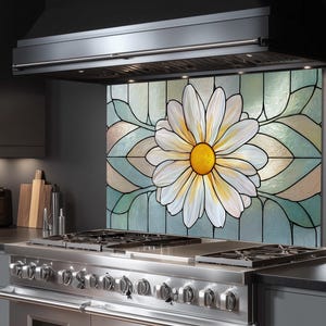 May include: A kitchen splashback with a large daisy design in a stained glass style. The daisy has white petals with yellow and black accents, set against a backdrop of pastel colours. The splashback is behind a stainless steel gas range.