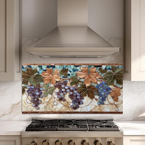 May include: A decorative kitchen backsplash featuring a mosaic design of grapes and leaves. The artwork showcases clusters of purple and blue grapes with brown and green leaves against a cream and teal background. The backsplash is framed with a brown border.