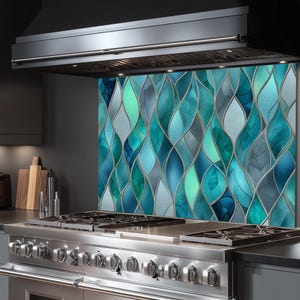 May include: A kitchen splashback with a stained glass design. The pattern features flowing, organic shapes in shades of teal, turquoise, and blue, outlined with silver. It's installed behind a stainless steel gas range and under a black cooker hood.