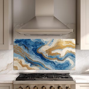 May include: A rectangular kitchen backsplash with an abstract design. The design features flowing patterns of blue, gold, and white, resembling marble or agate. The backsplash is installed above a gas range and below a stainless steel range hood.