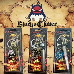 May include: Three Black Clover keychains in plastic packaging. Each keychain features a sword design and a character charm. The background includes the Black Clover logo and a map design. The keychains are silver and black.