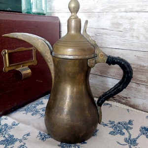 May include: A brass Arabic coffee pot with a black leather handle and a decorative finial on the lid.