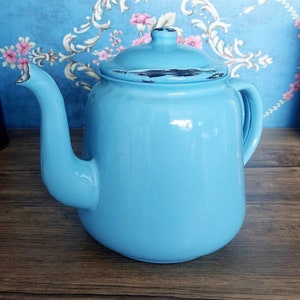 May include: A light blue enamel teapot with a slightly chipped lid. The teapot has a rounded body and a spout on one side and a handle on the other.