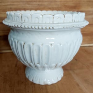 Op de afbeelding: Witte keramische plantenpot met een geribbeld ontwerp en een decoratieve rand. De pot heeft een brede basis en een smalle opening.