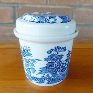 May include: A white ceramic jar with a blue and white willow pattern. The jar has a lid and is decorated with a traditional Chinese landscape scene.