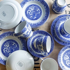 Pode incluir: Uma coleção de chávenas de chá e pires de porcelana azul e branca com um padrão tradicional de salgueiro. O conjunto inclui uma variedade de tamanhos e formas, incluindo uma chávena de chá e um pires, um prato pequeno e um prato maior.