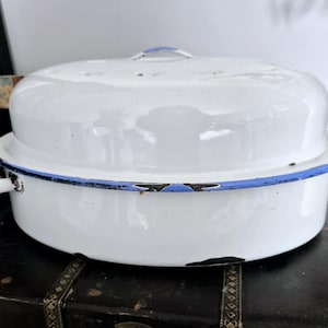 Peut inclure: Rôtissoire en émail blanc avec couvercle assorti. La poêle a un bord et des poignées bleus, et une poignée bleue sur le couvercle. La poêle montre des signes d'usure, ajoutant à son charme vintage. Un article de cuisine classique.