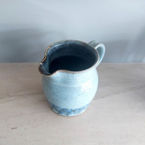 May include: A small, light blue ceramic pitcher with a dark blue glaze inside and a blue and white pattern around the bottom.
