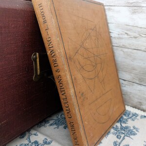 Könnte beinhalten: Ein braunes Vintage-Buch mit dem Titel "Foundry Calculations & Drawing - T. Booth". Das Buch hat ein geometrisches Design auf dem Umschlag.