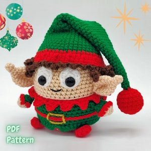 Pode incluir: Um brinquedo de elfo de crochê com um chapéu verde, roupas vermelhas e verdes e uma peruca castanho encaracolada. O elfo tem um rosto sorridente com olhos pretos e um nariz branco.