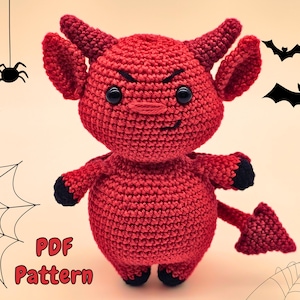 Peut inclure: Poupée diable rouge crochetée, avec des accents noirs sur les mains, les pieds et la queue pointue. Elle a des cornes et une expression renfrognée. Le fond présente des araignées, une toile et des chauves-souris. Le texte "PDF Pattern" est visible.