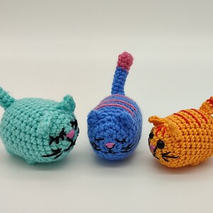 Front view of three crocheted kittens with their tails raised. Light blue, blue and orange.