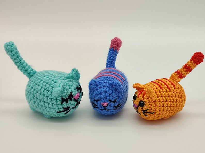 Front view of three crocheted kittens with their tails raised. Light blue, blue and orange.
