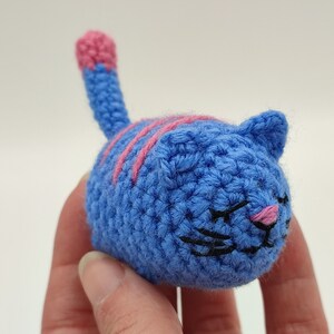 An blue and pink Amigurumi kitten, held in hand.