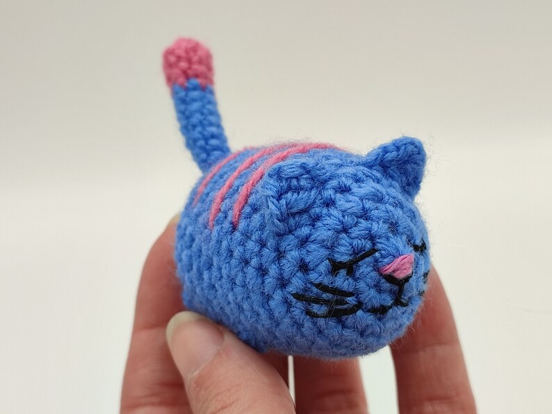 An blue and pink Amigurumi kitten, held in hand.