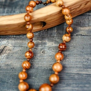 May include: A wooden bead necklace with brown and orange tones. The beads are round and have a natural wood grain pattern. The necklace is lying on a wooden surface.