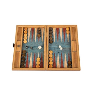 Puede incluir: Un tablero de backgammon de madera con una superficie de juego azul, puntas triangulares rojas y blancas y fichas de madera. Los dados están esparcidos por el tablero. El tablero está abierto y listo para jugar.