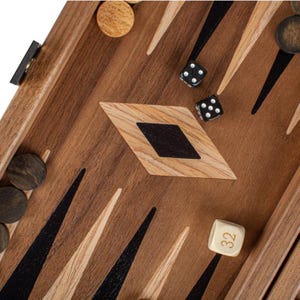 Pode incluir: Um tabuleiro de gamão de madeira com peças pretas e brancas. O tabuleiro tem um desenho em forma de diamante no centro. Há dois dados no tabuleiro, um com o número 6 e outro com o número 3. Há também um dado branco com o número 32 nele.