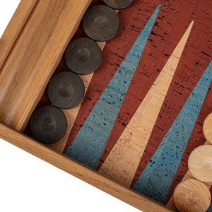 May include: A wooden backgammon board with a cork surface. The board has a red, blue, and beige pattern. There are black game pieces on the board.