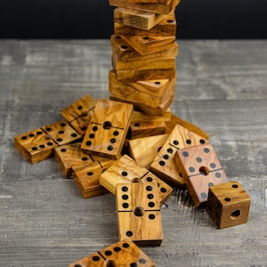 May include: A stack of wooden dominoes with black dots on a gray wooden surface. The dominoes are arranged in a random pattern, with some standing upright and others lying flat.
