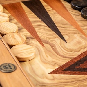 May include: A wooden backgammon board with a natural wood finish and inlaid triangles of different coloured wood. The board has a set of wooden playing pieces.